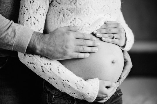 Cropped image of husband holding belly of his pregnant wife. Pregnant woman and loving handsome man hugging tummy at home. Loving Couple. Parenthood concept. Baby Shower. Black and white photo.