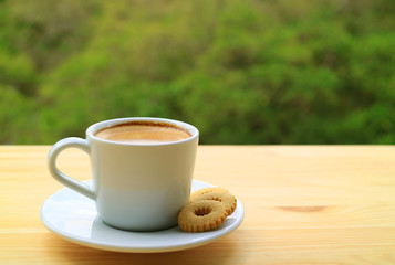 Cup of Hot Coffee and Cookies on Outdoor Wooden Table with Blurry Green Foliage in Background	