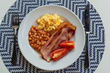 English breakfast with grilled bacon, tomatoes, scrambled eggs and baked beans in tomato sauce