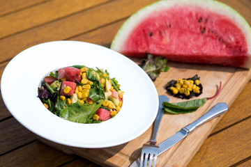 a plate of watermelon salad with avocado, corn and lettuce