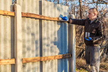 A man hand with blue glove holding paint brush applying wood lacquer. Man with work clothes and protective gloves paints a wooden board with a protective paint brush in a light workshop