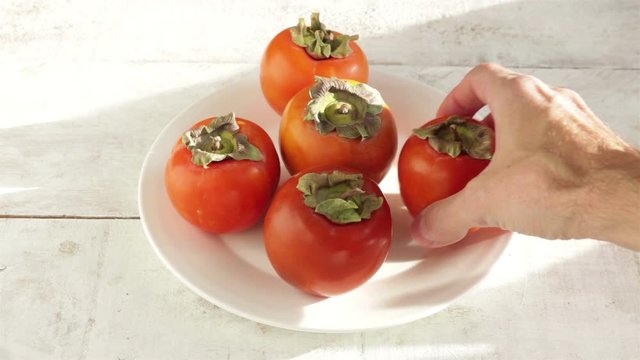 man and woman hand take a persimmon fruit from white plate close up