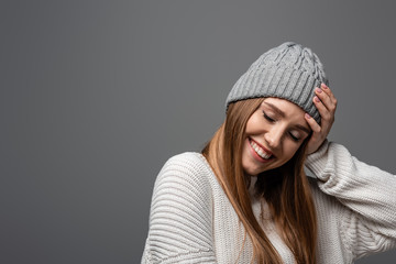 attractive smiling woman in knitted hat and sweater, isolated on grey