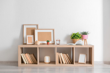 Stand with books and houseplants near white wall