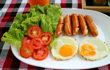 Plate of fried eggs and fried sausages with fresh salad for breakfast 