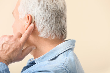 Mature man with hearing aid on light background