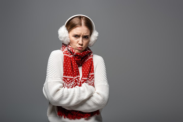 offended cold girl in white sweater, earmuffs and scarf posing with crossed arms, isolated on grey