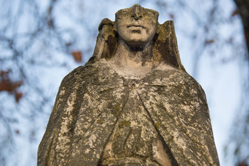Monument and candles in the cemetery. All Saints Day in Poland. Stone statue. Statue without a face.