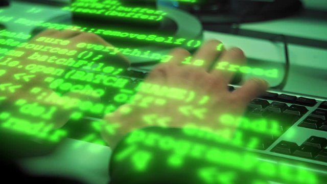 Green code characters fly by over typing haker's hands in a dark office room. Close-up shot. 4K (UHD)
