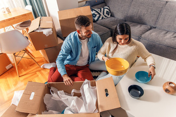 Smiling young couple move into a new home sitting on floor and unpacking.