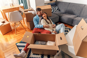 Smiling young couple move into a new home sitting on floor and unpacking.