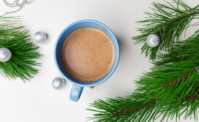 Obraz na płótnie Canvas Blue cup of hot cacao or cappuccino with cinnamon standing on white table with pine branches and silver bulbs. Merry Christmas, Happy New Year and winter holidays concept. Copy space.