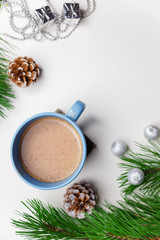 Obraz na płótnie Canvas Blue cup of hot cacao or cappuccino with cinnamon standing on white table with pine branches and silver bulbs. Merry Christmas, Happy New Year and winter holidays concept. Copy space. Vertical shot.