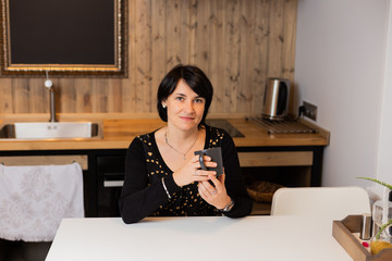 A beautiful woman of 50 years old is sitting in the kitchen in a modern interior and drinking tea. Woman portrait.