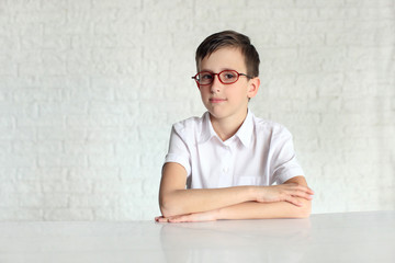 schoolboy in glasses sitting at desk with books and using laptop isolated on white
