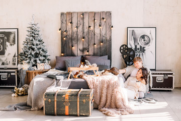 Happy family on Christmas. Mother and father sit on the floor with a drink & looking at the child. Little girl is lying on the bed. Parents love their daughter. New year 2020.