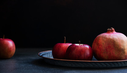 Still life of autumn red fruits, whole pomegranates and apples. Front view, black background, copy space
