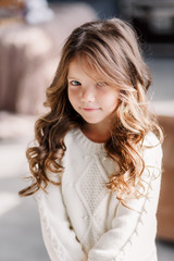 A little girl is sitting on the bed & posing on the eve of the new year 2020. Beautiful baby girl in a gray skirt and a white sweater.