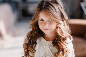 Obraz premium A little girl is sitting on the bed & posing on the eve of the new year 2020. Beautiful baby girl in a gray skirt and a white sweater.