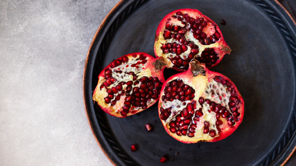 Sliced juicy pomegranate fruits on a vintage metal plate. Top view, gray marble background, copy space