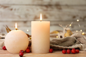 Glowing candles with berries and plaid on wooden table