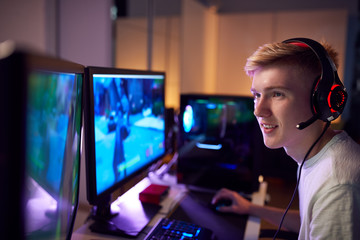 Teenage Boy Wearing Headset Gaming At Home Using Dual Computer Screens