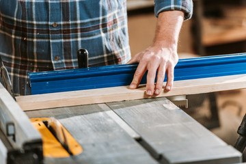 cropped view of woodworker holding plank near circular saw