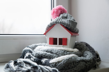 house in winter - heating system concept and cold snowy weather with model of a house wearing a knitted cap