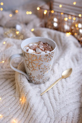 Obraz na płótnie Canvas Cup of hot cocoa with marshmallows and christmas lights on knitted plaid