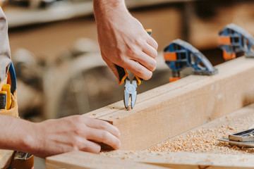 cropped view of carpenter holding pliers near wooden dowel