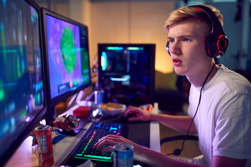 Fototapeta na wymiar Teenage Boy Wearing Headset Gaming At Home Using Dual Computer Screens