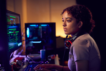 Female Teenage Hacker Sitting In Front Of Computer Screens Bypassing Cyber Security - obrazy, fototapety, plakaty