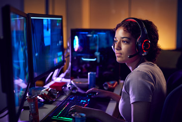 Teenage Girl Wearing Headset Gaming At Home Using Dual Computer Screens - obrazy, fototapety, plakaty