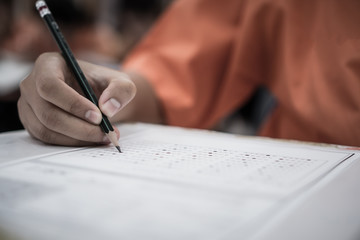 Exam test school or university concept : Hand student holding pencil writing standardized answer multiple carbon paper form with gray black answers sheet bubbled doing final assessment in classroom