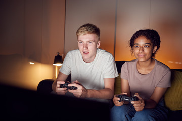 Teenage Couple Sitting On Sofa At Home Computer Gaming Together © Monkey Business