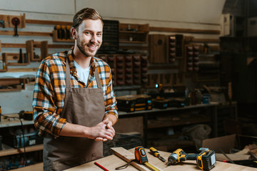 happy woodworker with clenched hands standing near table with tools