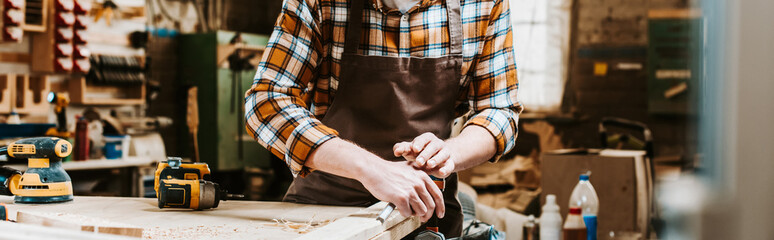 panoramic shot of woodworker holding chisel while carving wood in workshop