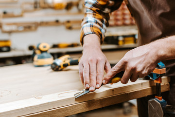 cropped view of carpenter cutting wooden plank