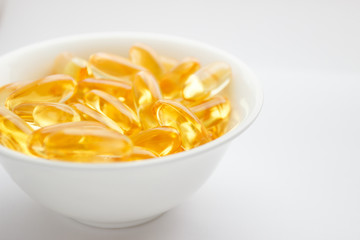 Dietary supplementation. Capsules of fish oil in the white bowl, light background