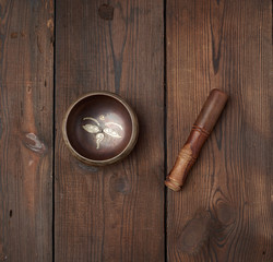 singing Tibetan copper bowl and wooden stick on a table of brown boards