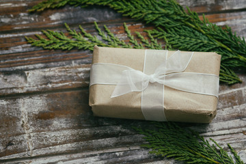 Gift box wrapped in brown craft paper and tie white satin ribbon. Christmas mood. Decorative wood background. Present package.	