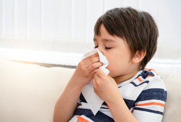 Unhealthy kid blowing nose into tissue, Child suffering from running nose or sneezing , A boy...