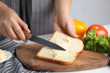 Woman spreading butter on sandwich at white table, closeup
