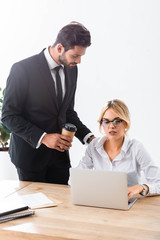 Fototapeta premium Businessman with coffee looking at colleague working with laptop