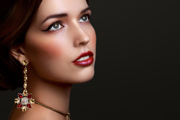 Beautiful girl with red lipstick and golden jewellery earrings isolated on a dark background