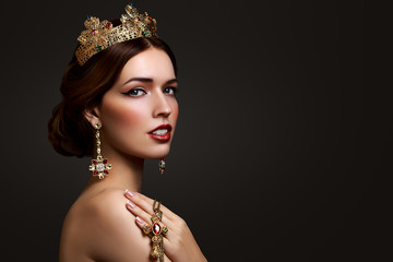 Beautiful girl with red lipstick in golden crown and earrings on dark background