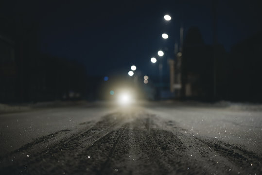 Empty snowy winter road at night time and car headlight background. Blurred image.