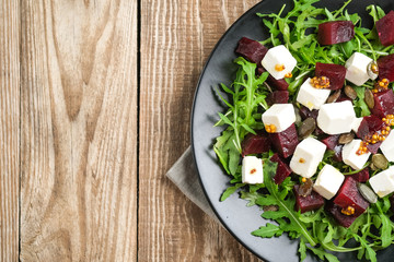 Salad with beetroot, feta cheese, arugula and spicy dressing on a rustic background top view. Healthy food. Top view. Copy space.