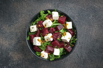 Salad with beetroot, feta cheese, arugula and spicy dressing on a dark background top view. Healthy food. Top view. Copy space.