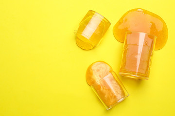 Overturned plastic containers with bright slimes on yellow background, top view. Space for text